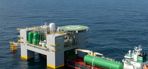 Offshore-Wasserstoffproduktionsplattform mit Windturbinen, die grünen Wasserstoff erzeugt. Ein Transportschiff wird beladen.