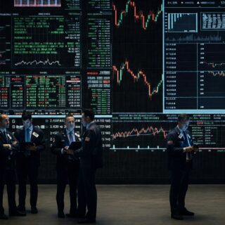 Börsenparkett mit digitalen Kursanzeigen und Menschen, die Aktienkurse diskutieren.