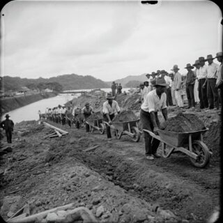 Schwarz-Weiß Fotografie, die den Bau des Panamakanals zeigt, mit Arbeitern, Maschinen und unvollendeten Kanalstrukturen in einer dynamischen Baustelle.