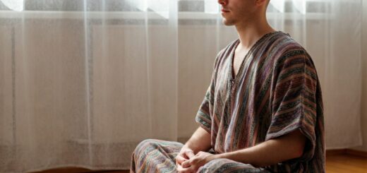 Das Bild zeigt eine entspannte Person, die in einem ruhigen, lichtdurchfluteten Raum sitzt und meditiert. Im Hintergrund sind nur leise andeutungsweise technische Geräte zu sehen, die ausgeschaltet sind, um den Fokus auf den Zustand der inneren Balance und Erholung zu legen. Das Bild vermittelt eine realistische, entspannte Atmosphäre, passend zum Thema Digital Detox.