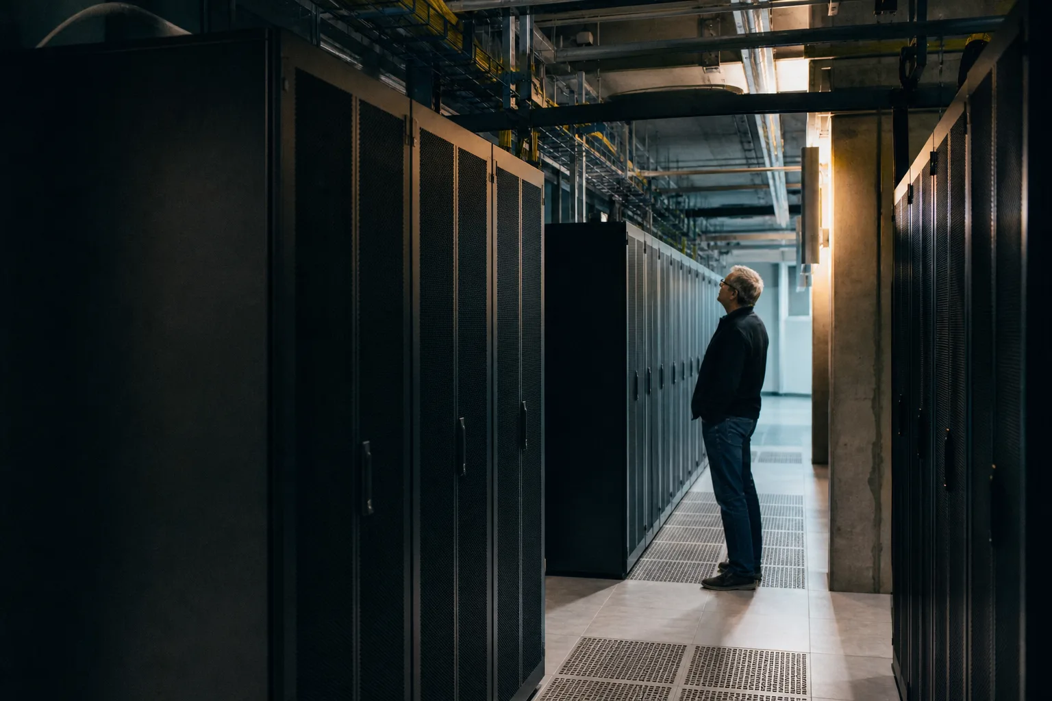 Eine Ingenieurin steht in einem neutralen Rechenzentrum zwischen unbeschrifteten Serverracks.