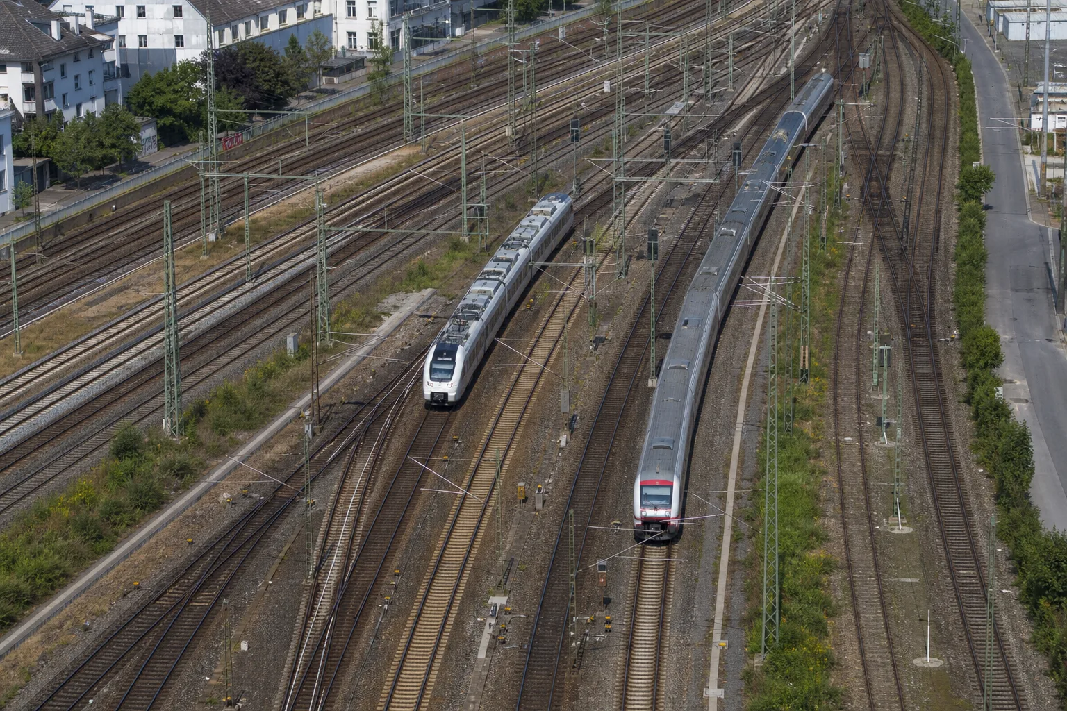 Aus der Luft sind mehrere elektrifizierte Gleise, Weichen und zwei neutrale Personenzüge an einem dicht genutzten Bahnknoten zu sehen.
