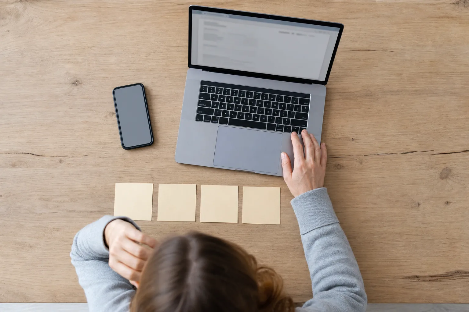 Hände prüfen am Tisch eine Nachricht auf Smartphone und eine selbst geöffnete Website am Laptop.