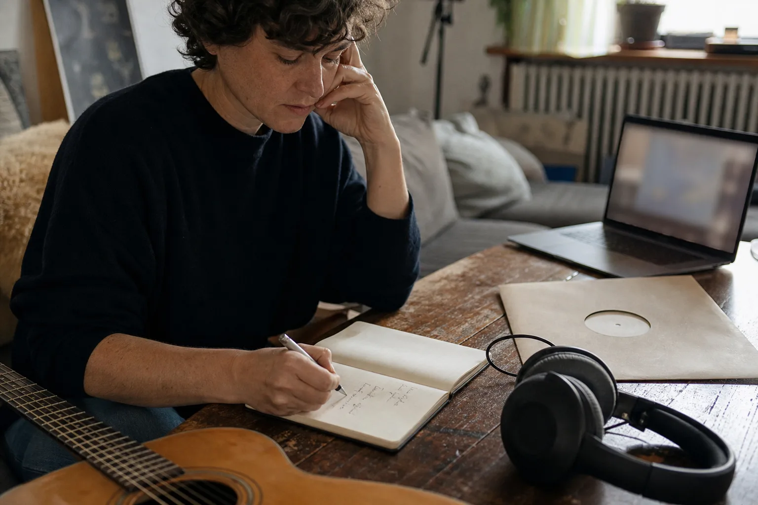 Musikbegeisterte Person mit Kopfhörern, Gitarre und Notizbuch in einem Wohnzimmer
