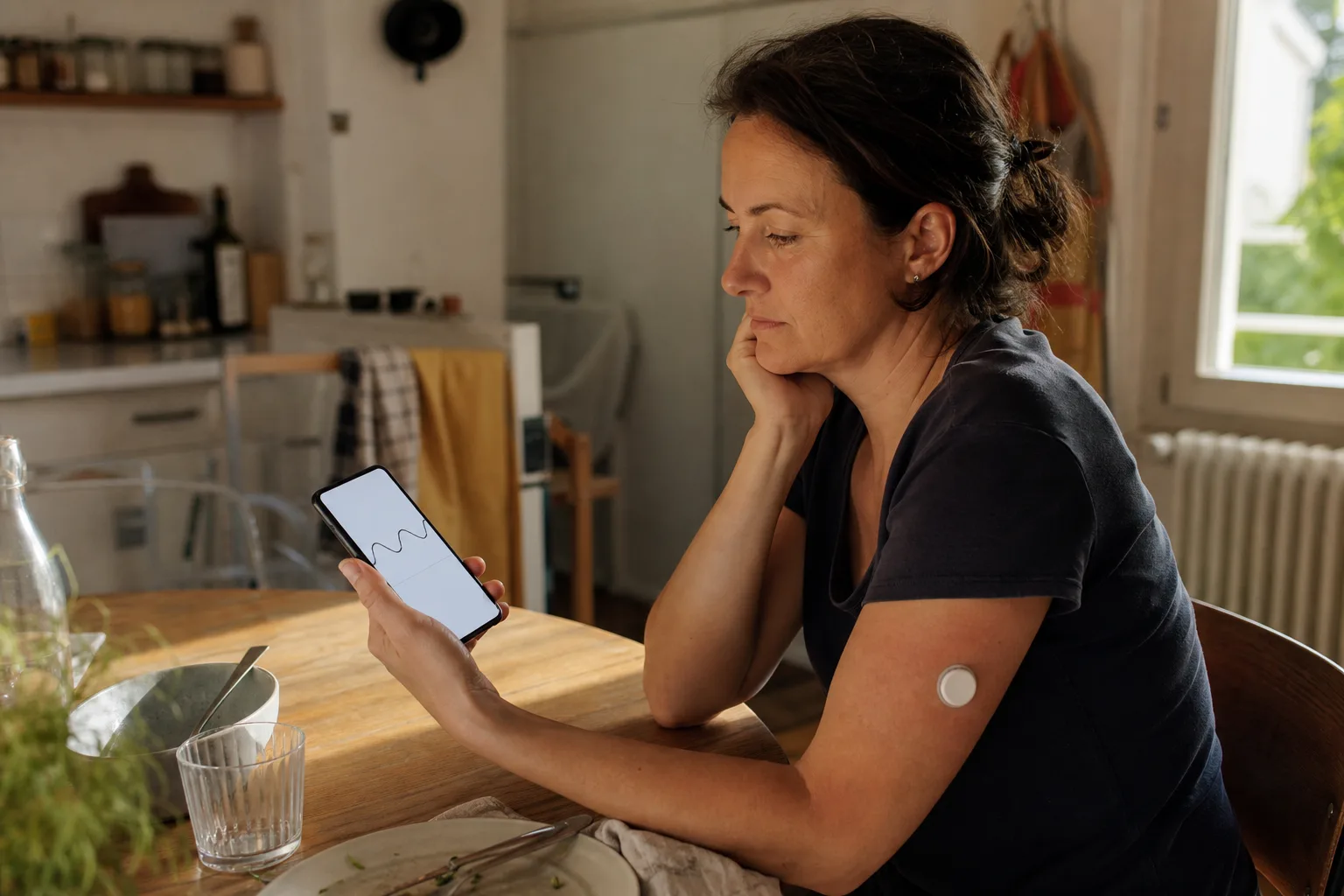 Person betrachtet nach einer Mahlzeit eine Glukosekurve auf einem Smartphone, während ein diskreter Sensor am Oberarm sichtbar ist