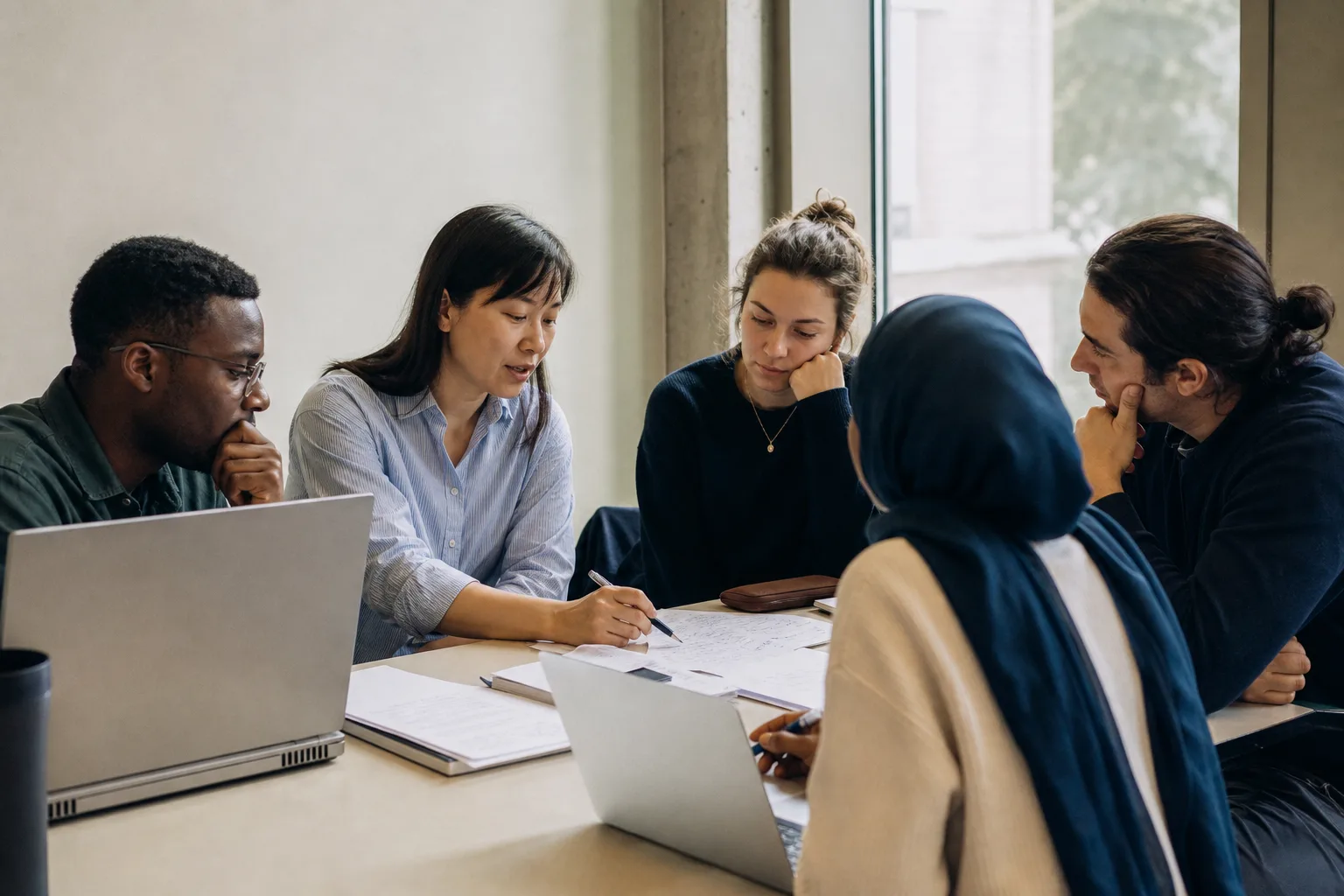 Studierende und eine Lehrperson besprechen generative KI an einem Hochschulseminartisch mit neutralen Laptops