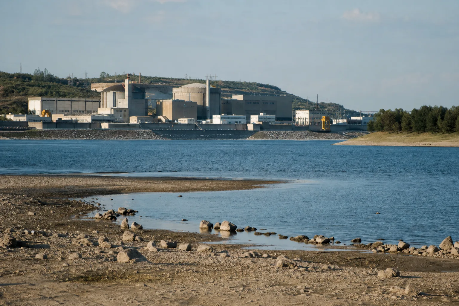 Niedriger Flusspegel und trockene Uferkante vor einem generischen Flusskraftwerk in Südosteuropa