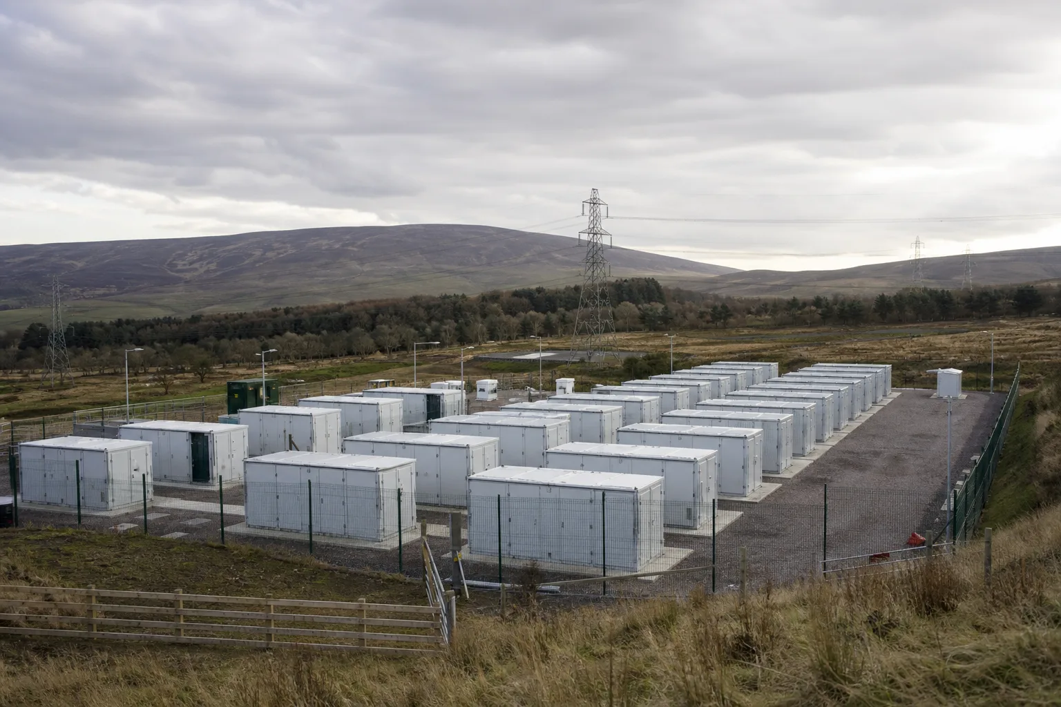 Netzgekoppelte Großbatterieanlage mit Containerreihen und Strommasten in einer schottischen Landschaft