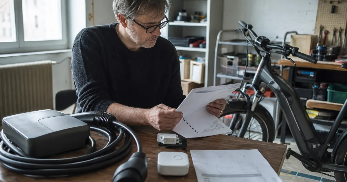 Person vergleicht an einem Arbeitstisch die Anschlüsse und Unterlagen einer Wallbox neben einem E-Bike