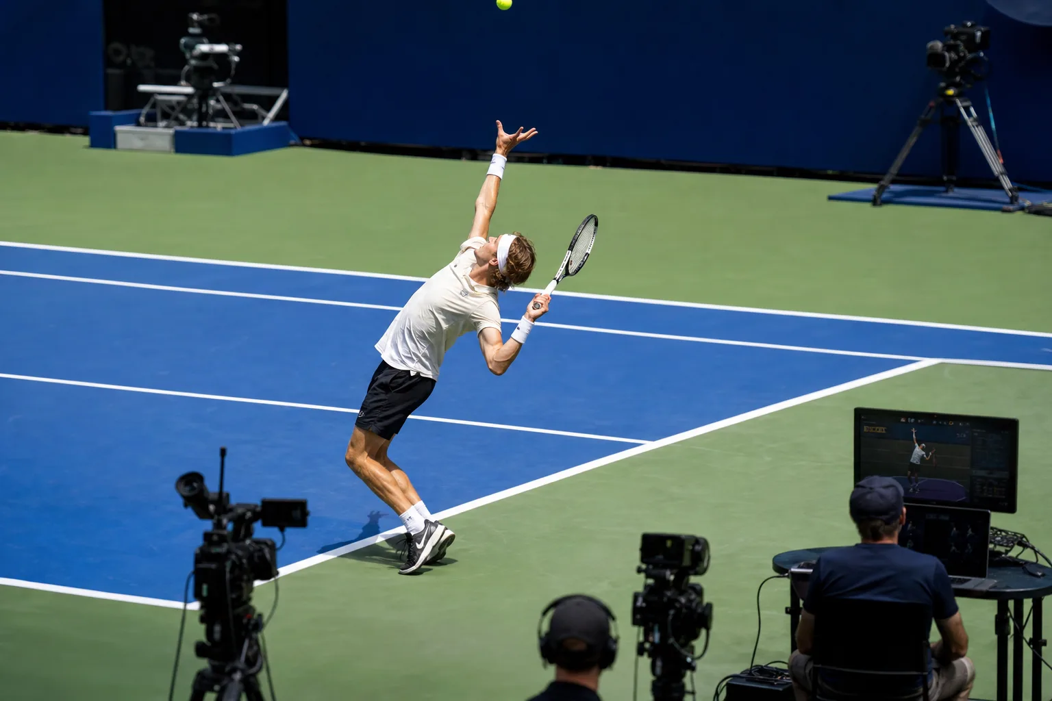 Tennisspieler beim Aufschlag auf einem Hartplatz mit unaufdringlicher Kameraanalyse im Hintergrund
