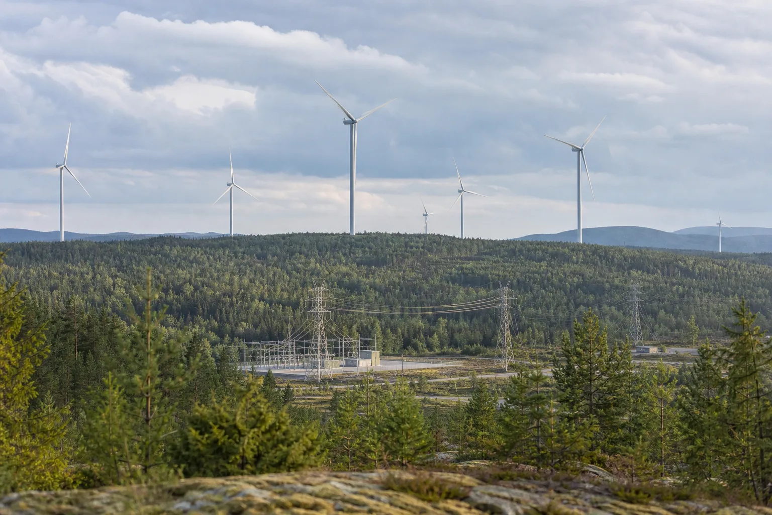 Schwedische Onshore-Windparks auf bewaldeten Hügeln mit räumlich getrennter neutraler Netzinfrastruktur im Hintergrund.