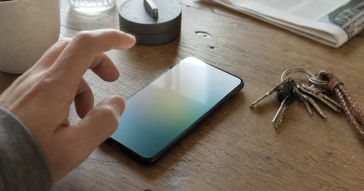 Unmarkiertes Smartphone neben Küchentimer und Schlüsselbund auf einem benutzten Tisch