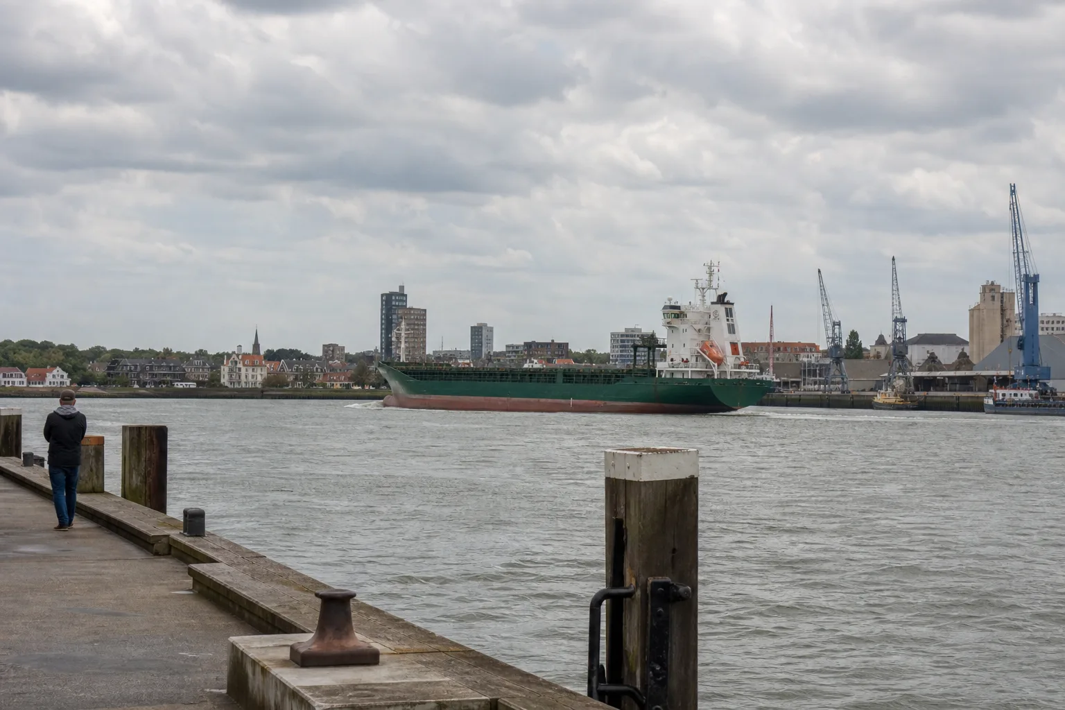 Frachtschiff auf einer Nordseeroute vor Hafenanlagen und einer bewohnten Küste