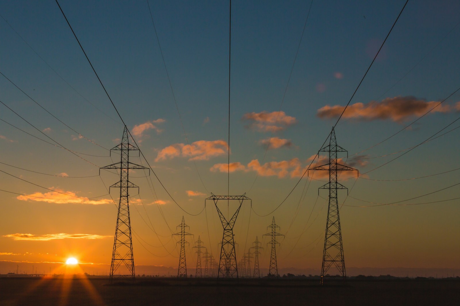 Hochspannungsmasten in langer Reihe vor orangefarbenem Sonnenuntergang – Symbolbild für Stromnetz und Versorgungssicherheit