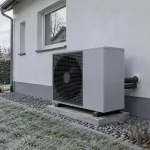 Stromzähler und Außengerät einer Luft-Wasser-Wärmepumpe an einem Einfamilienhaus bei winterlichem Tageslicht